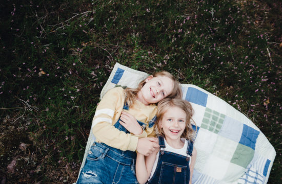 Syskonfotografering med systrar som ligger på filt bland ljung